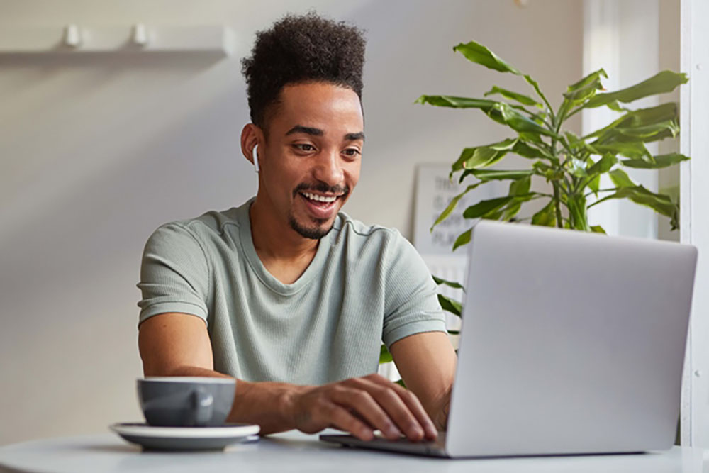 photo young attractive african american joyful boy works laptop sits cafe looks monitor broadly smiling chating with his girlfriend 1